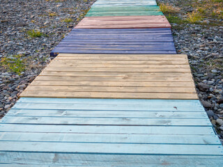 Multi-colored decking on a pebble beach. The path to the shore from different colored boards.   Beach infrastructure. Road for the convenience of vacationers