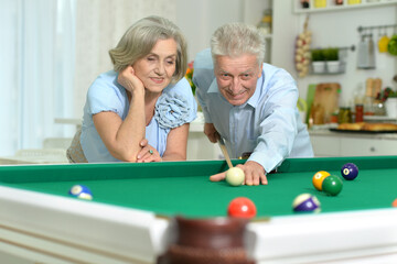 Happy senior couple playing billiards together in home