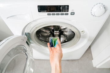 woman put laundry gel capsules in washing machine indoors, cropped shot