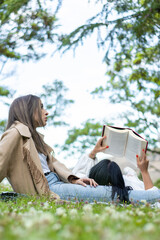 Girl lying on her friend legs while reading a book on the grass. Lifestyle of a girl lying on her friend's legs reading a book in the field