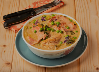 Creamy chicken and bacon with vegetables on a wooden surface.