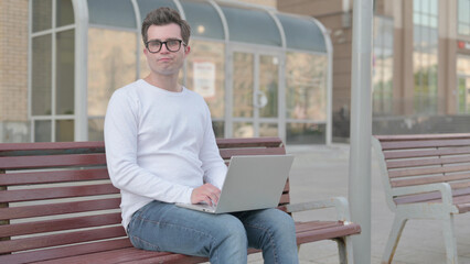 Rejecting Young Man in Denial While using Laptop Sitting Outdoor on Bench