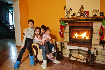 Happy four kids at home by a fireplace in warm living room on winter day.