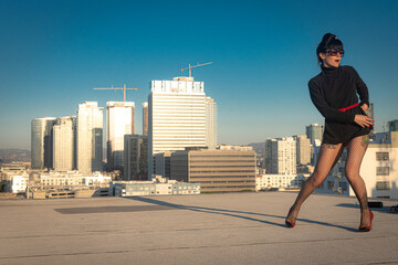 Glamorous tattooed woman in fishnet stockings and high heels poses on a Downtown Los Angeles Rooftop