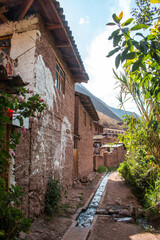 Fototapeta na wymiar Typical adobe houses with plants next to the water canal, between mountains in the village of Urquillos. Sacred Valley, Peru. 