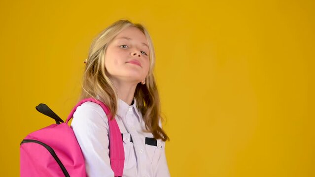 Portrait of a happy teenage schoolgirls in a school uniform with a backpack smiling on a yellow studio background. back to school concept	