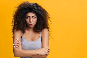 COOL OFFER. Upset pretty Latin female with afro cross hands, posing closed, look to camera, have hard feelings, stay isolated over yellow background. Copy space, free place