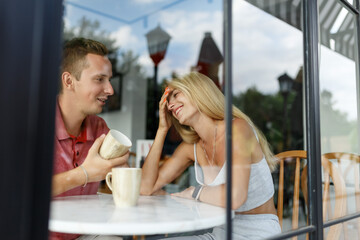Romantic loving couple drinking coffee, having a date in the cafe, view through window.