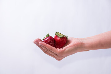 Obraz premium delicate hand holding two red strawberries, fruit, healthy living, lifestyle, healthy lifestyle