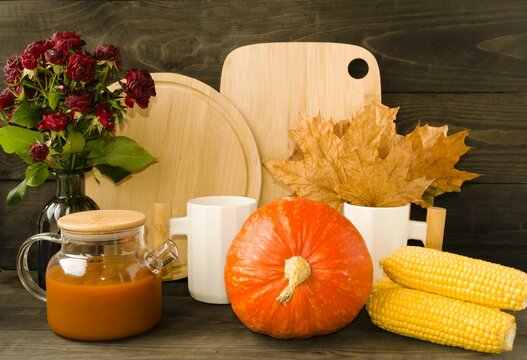 Home decor for Halloween holiday.  On a wooden background, a bright juicy pumpkin, wooden boards, kitchen utensils, autumn flowers, a kettle with pumpkin juice.  Front view.