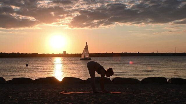Slow motion video of a young woman doing yoga workout on Baltic sea coastline during subset