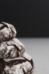Food photo of freshly baked Chocolate Crinkle Cookies. Close up macro image of stack of chocolate iced biscuits. Black and white background with copy space available