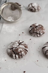 Food photo of freshly baked Chocolate Crinkle Cookies. Angle view of a chocolate iced biscuits on top of baking paper. Baking utensils, ingredients and tools in frame. Copy space available
