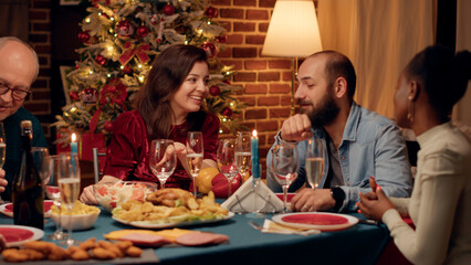Joyful wife and husband talking at home while enjoying Christmas dinner together. Lovely happy multiethnic group of people being festive while celebrating winter holiday.