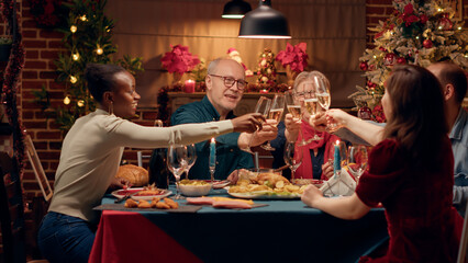 Happy close family members clinking champagne glasses while sitting together at Christmas dinner...