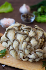 Fototapeta premium close-up Fresh organic healthy oyster mushrooms with green parsley, garlic, black pepper and pink salt on the wooden table. Delicious oyster mushrooms on a cutting board. copy space. vertical