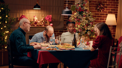 Happy diverse family members enjoying traditional home cooked food wihle celebrating winter holiday together. Cheerful people enjoying Christmas dinner while eating roasted chicken. Tripod shot