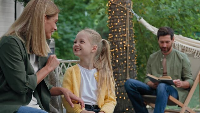 Caucasian mother talking laughing with funny daughter touching baby nose small kid girl running hugging dad by neck cuddling to bearded father reading book family outdoors recreation rest in camping