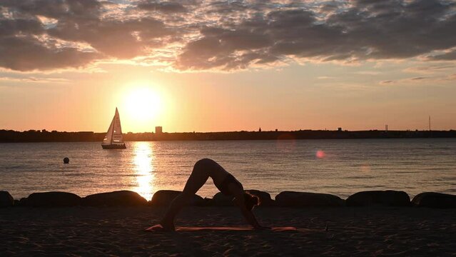 Slow motion video of a young woman doing yoga workout on Baltic sea coastline during subset