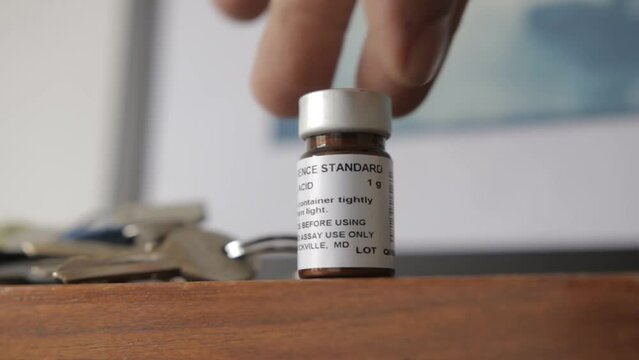 A man put a vial with reference standard material from ascorbic acid also known as vitamin C over a table
