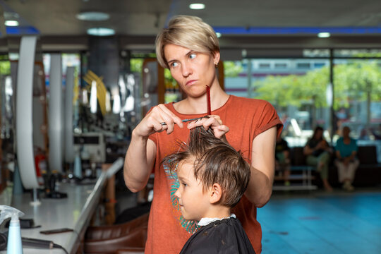Woman hairdresser trying on cut length of hair to boy client in barbershop salon