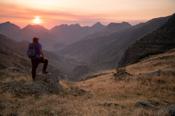 man standing on a mountain summit looking to the red sunset