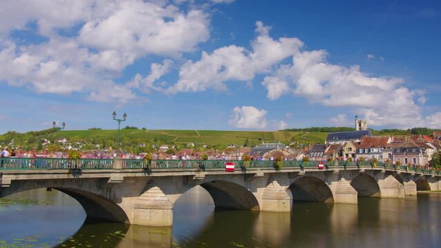 A large crowd of people on the bridge. Traffic from people. Time lapse. Beautiful clouds in the background of the old bridge. View of city landscape of Joigny on River Yonne, Burgundy, France