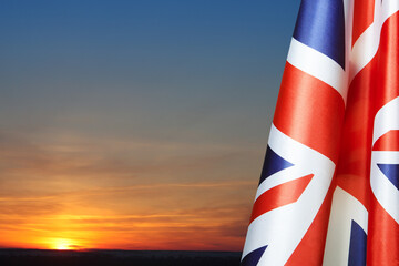 National flags of United Kingdom on a flagpole on sunset sky background. Lowered UK flags. Background with place for your text.