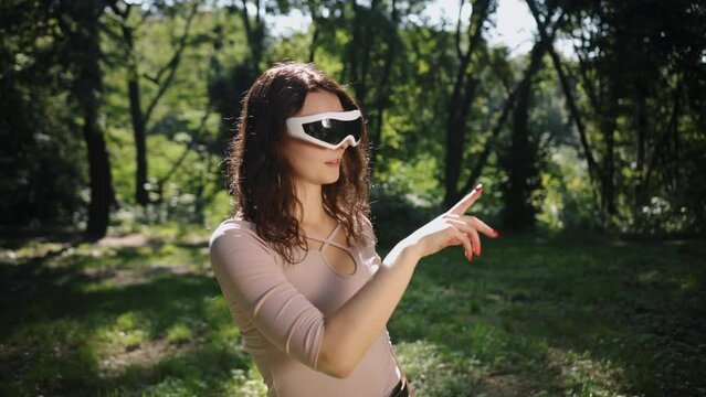 World of boundless imagination blended with nature perfectly in the future, beautiful woman with touch screen and virtual reality standing on the grass in an outdoor park.