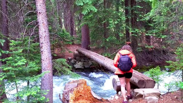 Young woman hiker hiking walking across creek crossing river in forest on conundrum hot springs trail Colorado with log wood bridge in wilderness