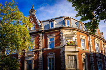 red brick tenement building with a small balcony, a tree, and with blue sky, european style city building, kamienica © Lukasz Czajkowski