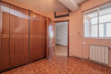 Room with a cabinet with bright wooden doors in a vintage look, an aluminum window in one corner and imitation wood stoneware floors