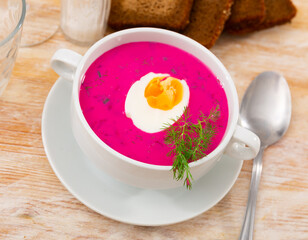 Traditional Russian Holodnik, cold yogurt beetroot soup with cucumber decorated by egg and dill served on table with cutlery