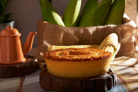 Homemade round cake made of green corn and cheese, known as "Pamonha Cake". Typical Brazilian food of Festa Junina(june festival) with a piece cut on a round wooden board on a rustic wooden table