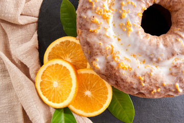 Traditional Brazilian orange cake with orange and lemon zest topping on a stone table and white brick rustic background. Orange slices and orange leaves on the side. Top View