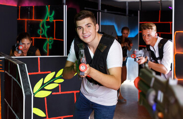 portrait of happy young men and women playing emotionally laser tag game in arena