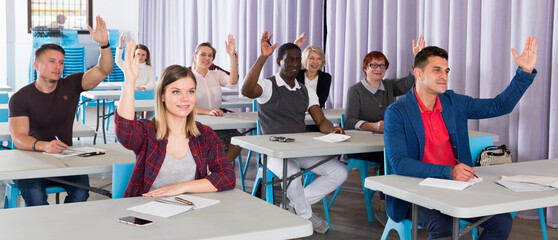 Portrait of multinational student group with hands raised during lesson in auditorium
