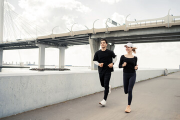 A sporty couple running down the street, fitness training running in sneakers. They use a fitness watch on their arm.