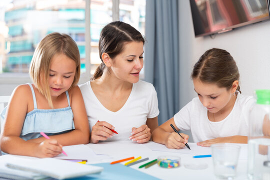 Two little girls with mother drawing together at home