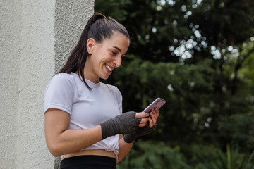 Portrait of a woman leaning against the wall texting on her cell phone after her exercise routine.