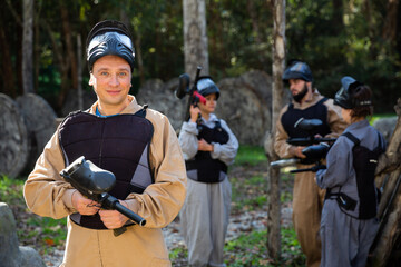 Fototapeta premium Portrait of male paintball sport player holding shooting gun and his team on background