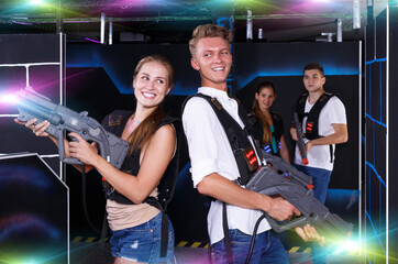 Fototapeta na wymiar Excited team of laser tag winners guy and girl with laser pistols and losers team in background