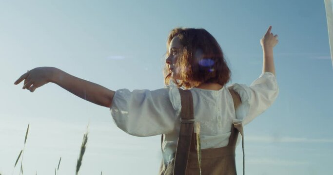 Young woman makes beautiful passes with her hands, posing for photography while standing among high wheat ears in a sunny summer day. 4k video, red komodo