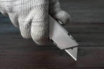 Man using utility knife at wooden table, closeup