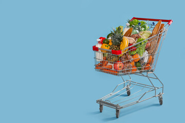 Shopping cart full of groceries on light blue background. Space for text - obrazy, fototapety, plakaty