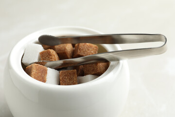 Different refined sugar cubes in bowl on light table, closeup
