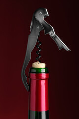 Opening bottle of wine with corkscrew on burgundy background