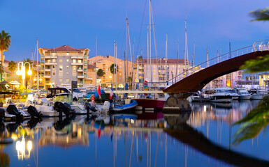 Picturesque evening view of coastal area of Frejus with comfortable residential buildings along illuminated quays and port for pleasure boats in summer, France