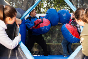 Obraz premium Happy male friends fighting by big stuffed boxing gloves at outdoor amusement playground