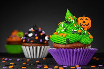 Halloween cupcake. Pumpkin Jack o lantern. Dessert on Halloween party. Muffin decorated with colored frosting and Icing shaped pumpkin Jack-o-lantern. Cupcakes on wooden black background. High quality